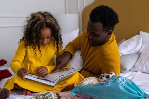 Photo by cottonbro studio on Pexels.com.  Father with daughter, father pointing to a book.  Support of reading is more than sounding out a word.